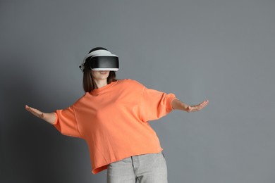 Woman using virtual reality headset on gray background, space for text