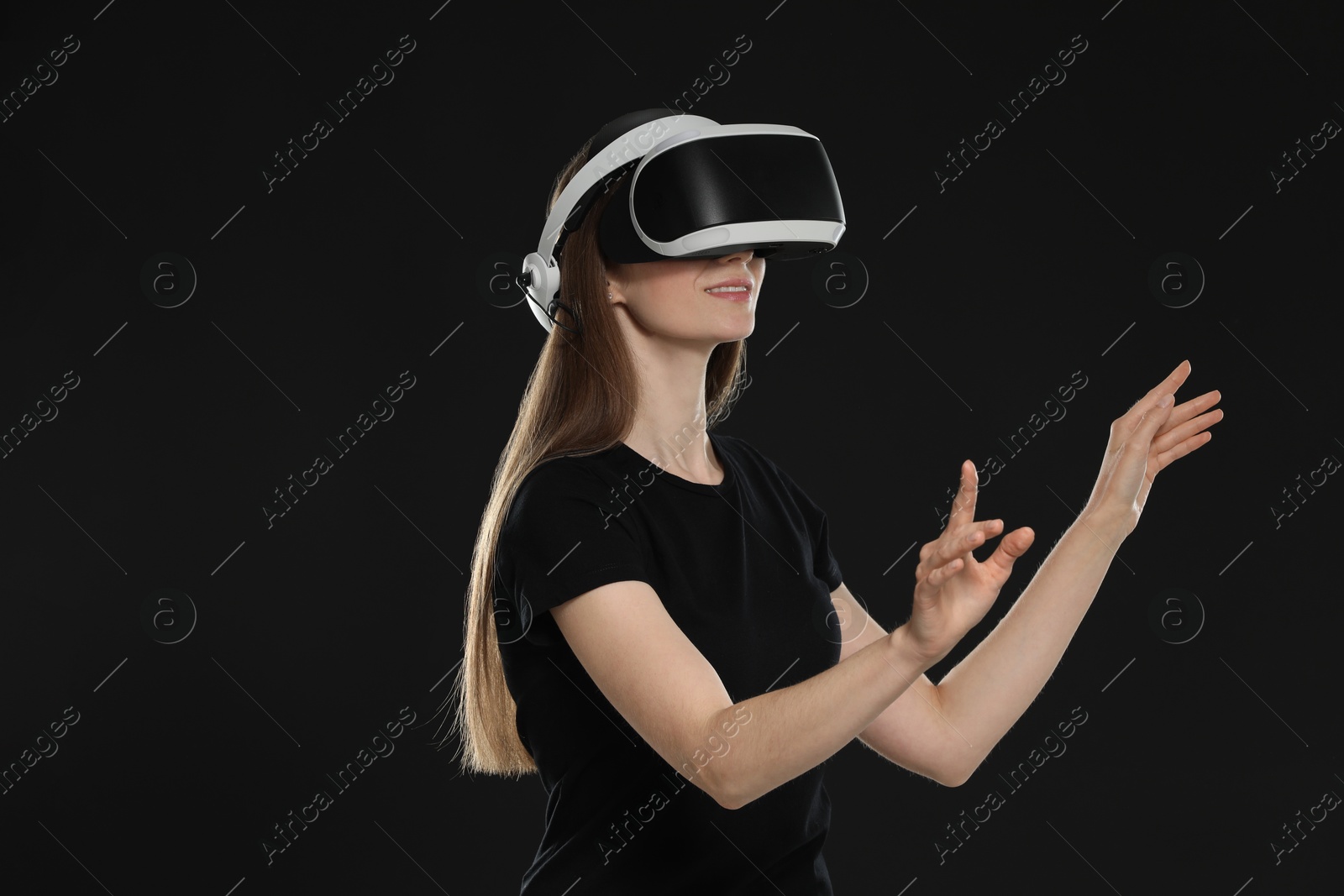 Photo of Smiling woman using virtual reality headset on black background, space for text