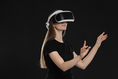 Photo of Smiling woman using virtual reality headset on black background, space for text