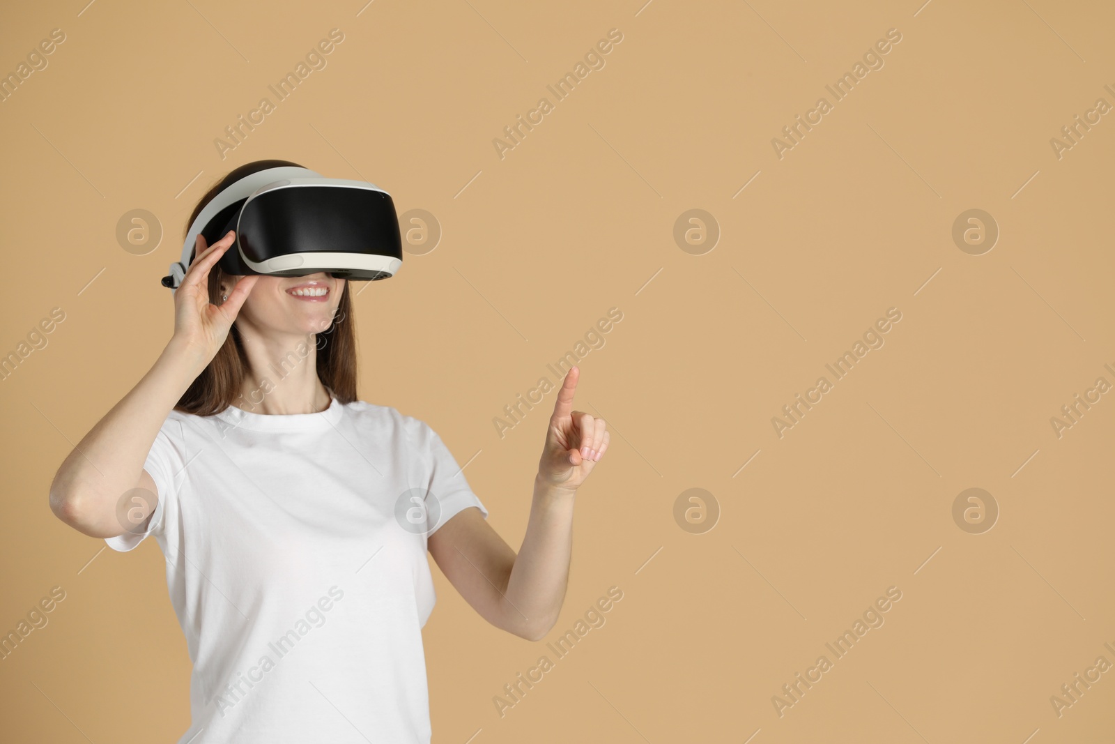 Photo of Smiling woman using virtual reality headset on beige background, space for text