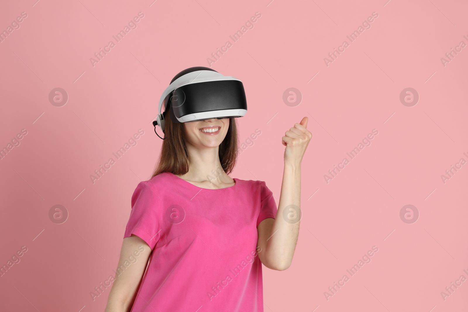 Photo of Smiling woman using virtual reality headset on pink background