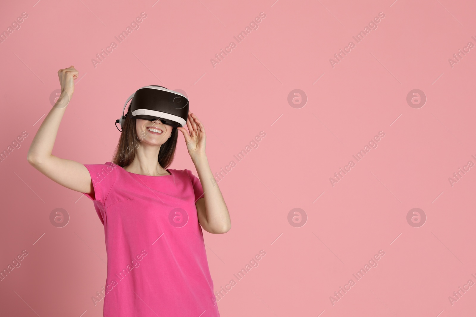 Photo of Smiling woman using virtual reality headset on pink background, space for text