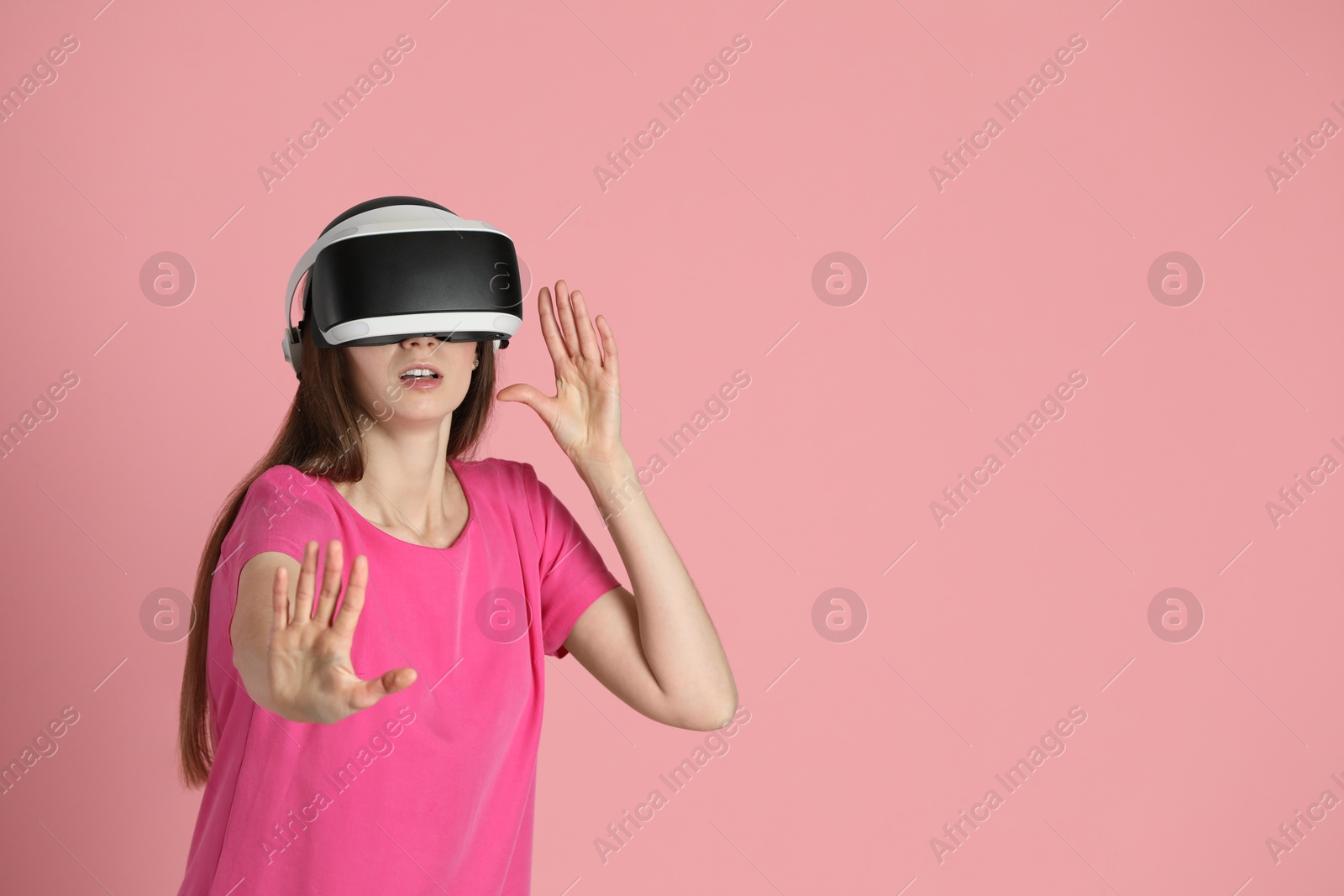Photo of Surprised woman using virtual reality headset on pink background, space for text