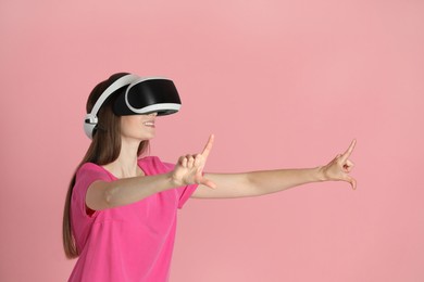 Photo of Smiling woman using virtual reality headset on pink background