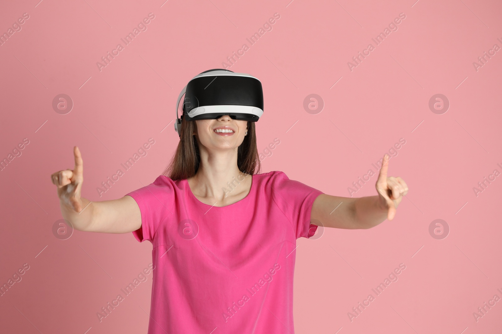 Photo of Smiling woman using virtual reality headset on pink background