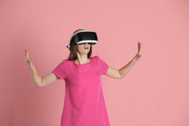 Surprised woman using virtual reality headset on pink background