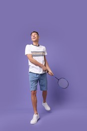 Photo of Young man playing badminton with racket on purple background, low angle view