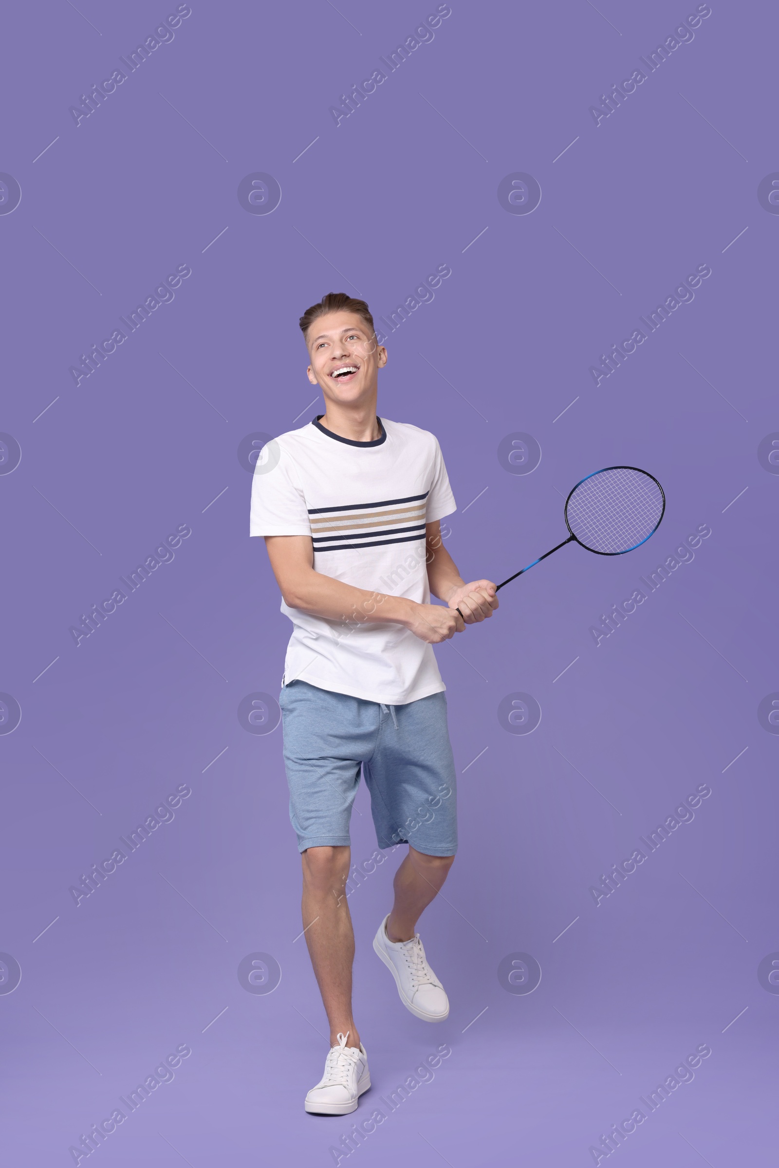 Photo of Young man playing badminton with racket on purple background