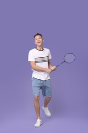 Young man playing badminton with racket on purple background