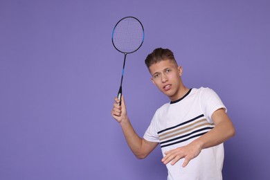 Young man playing badminton with racket on purple background, space for text