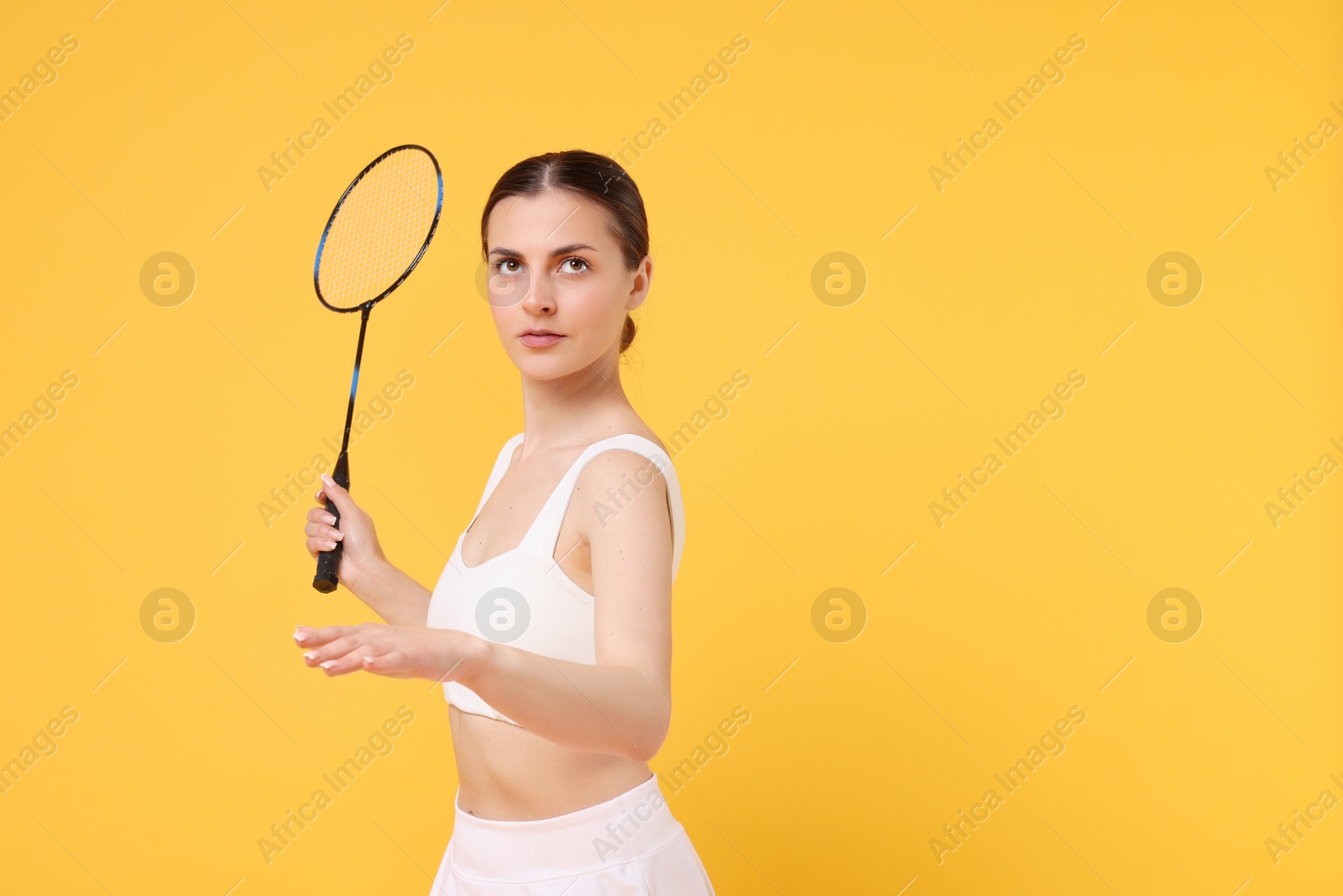 Photo of Young woman with badminton racket on orange background, space for text