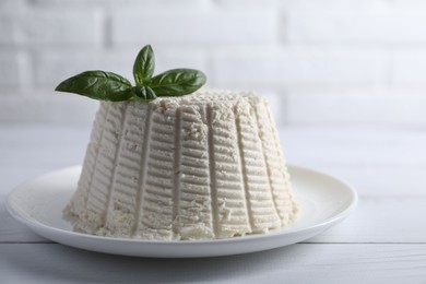 Fresh ricotta (cream cheese) with basil on white wooden table, closeup