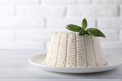 Fresh ricotta (cream cheese) with basil on white wooden table, closeup. Space for text