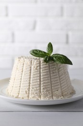 Photo of Fresh ricotta (cream cheese) with basil on white wooden table, closeup