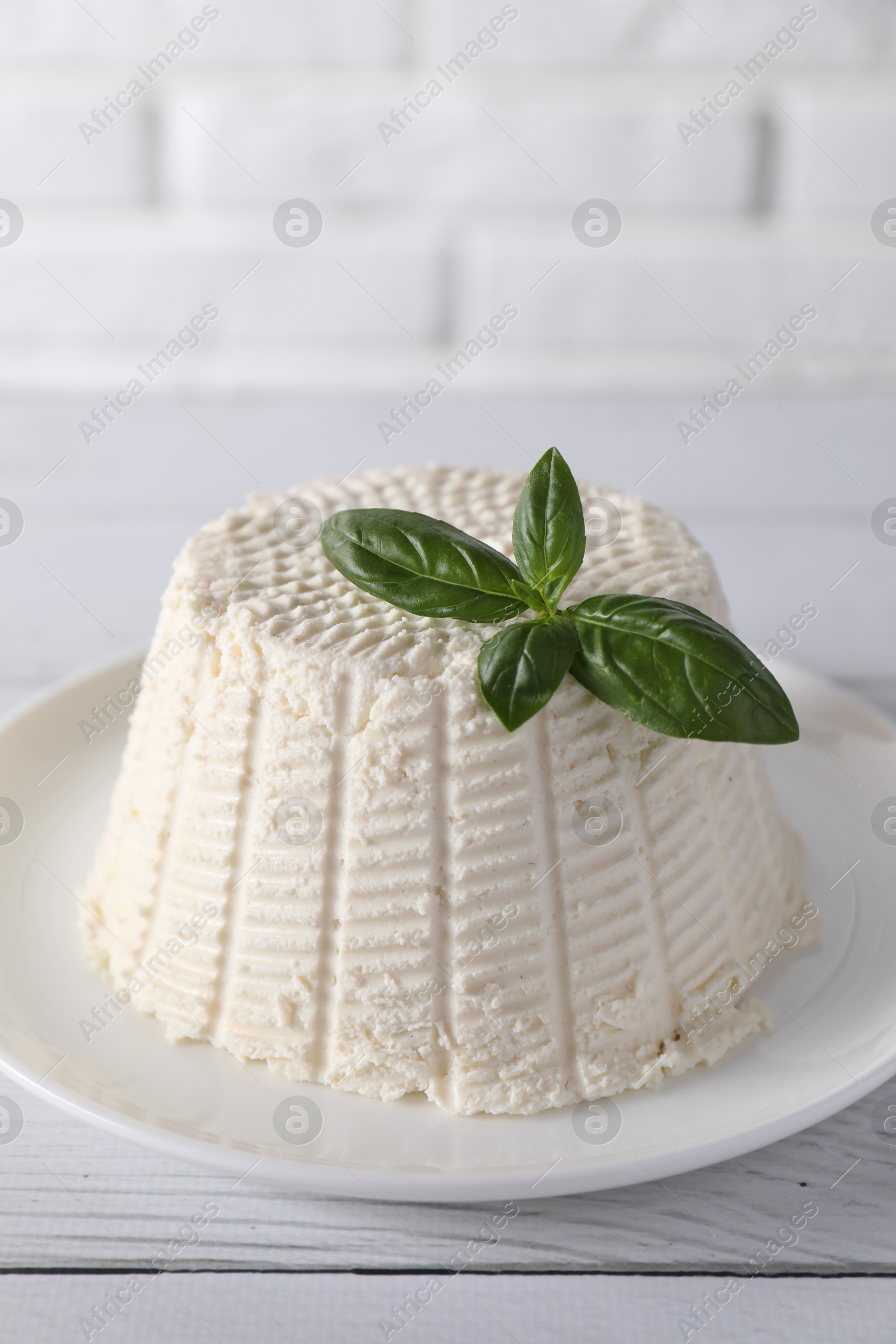 Photo of Fresh ricotta (cream cheese) with basil on white wooden table, closeup