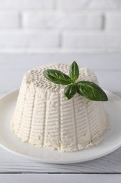 Photo of Fresh ricotta (cream cheese) with basil on white wooden table, closeup