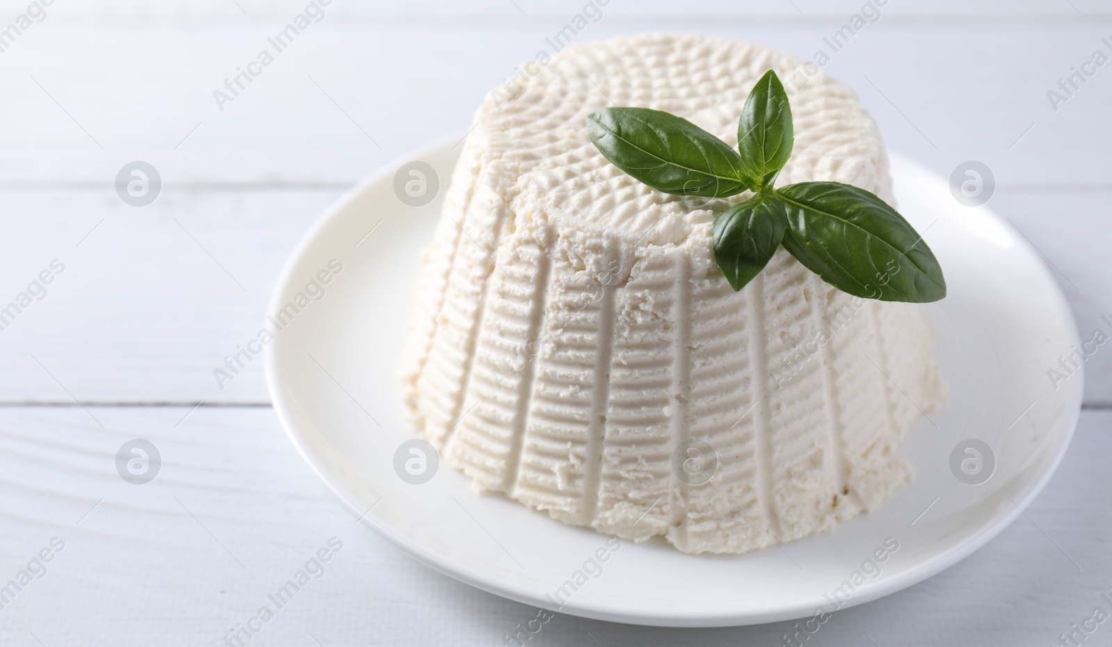 Photo of Fresh ricotta (cream cheese) and basil on white wooden table