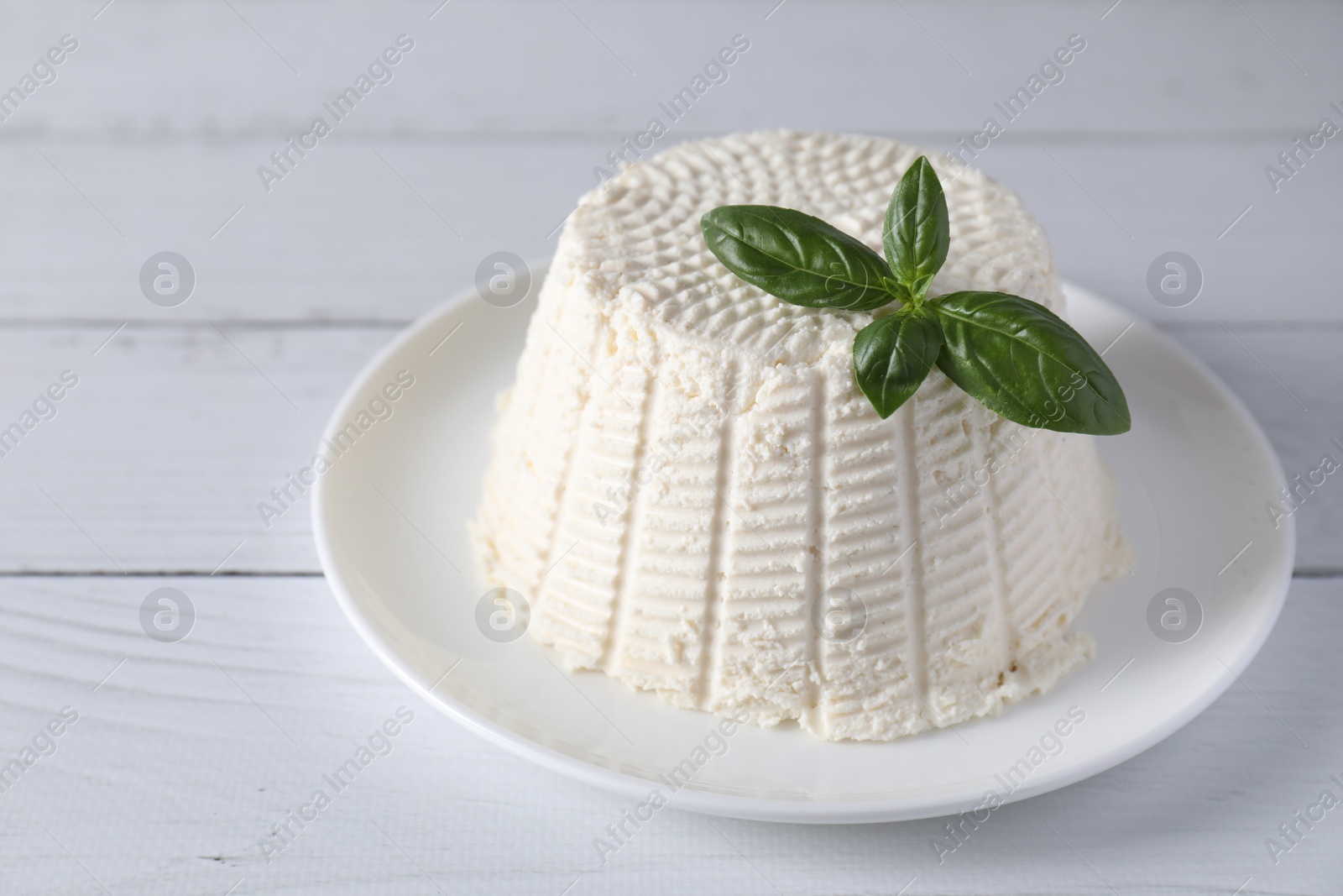 Photo of Fresh ricotta (cream cheese) and basil on white wooden table