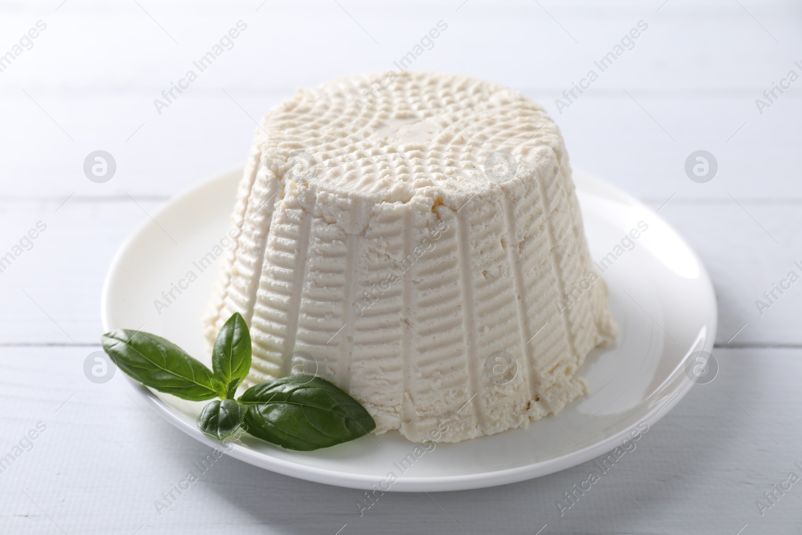 Photo of Fresh ricotta (cream cheese) and basil on white wooden table