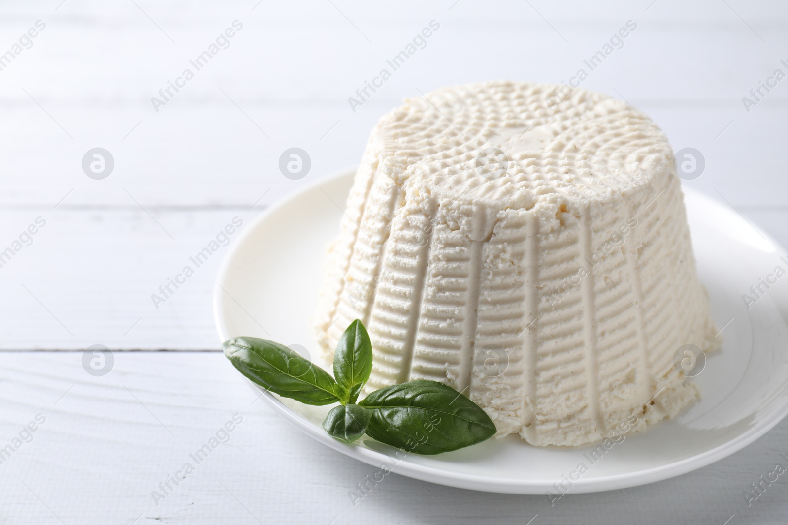 Photo of Fresh ricotta (cream cheese) and basil on white wooden table