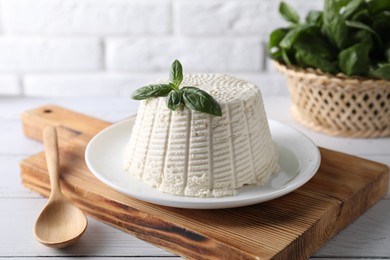 Photo of Fresh ricotta (cream cheese) with basil and spoon on white wooden table