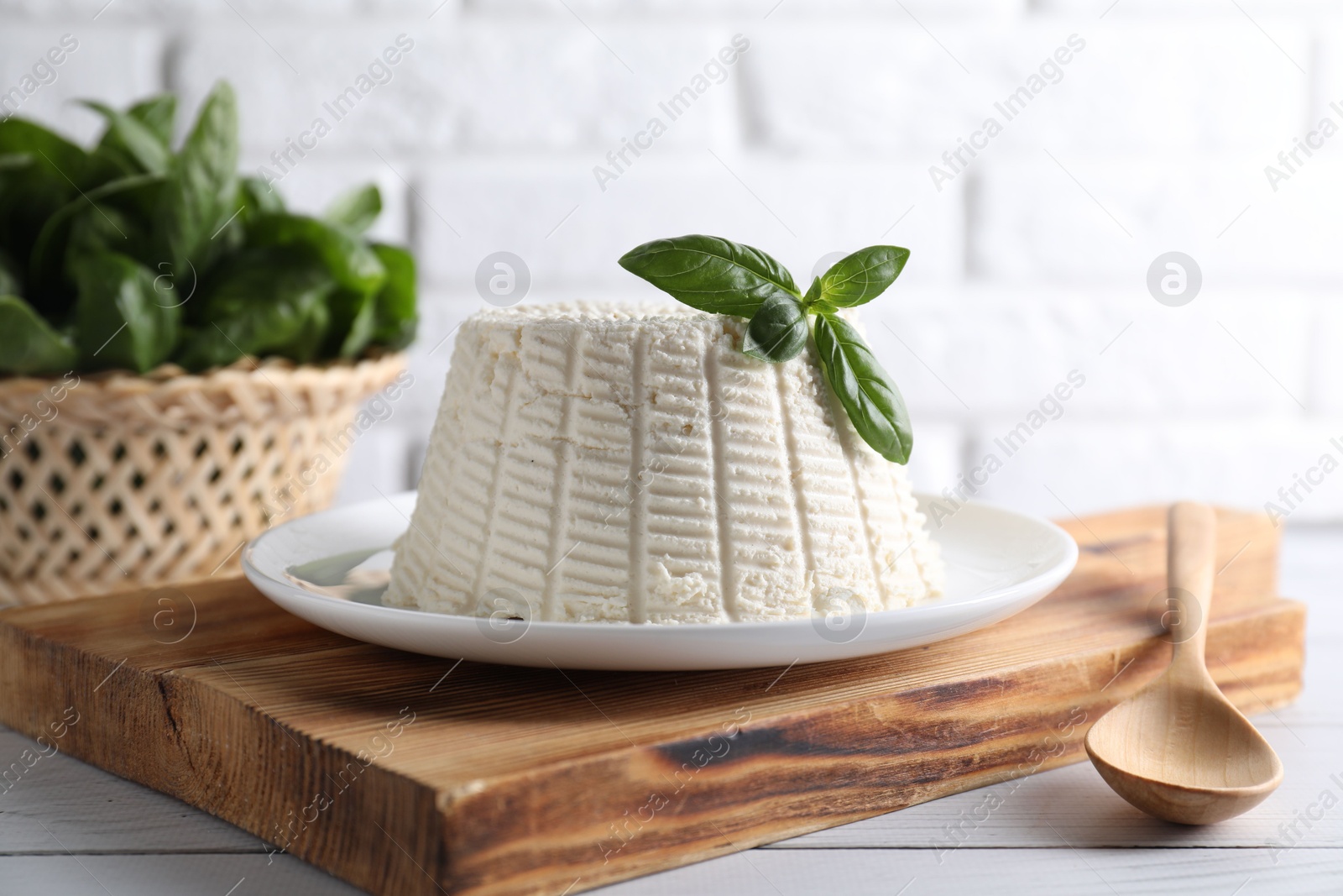 Photo of Fresh ricotta (cream cheese) with basil and spoon on white wooden table