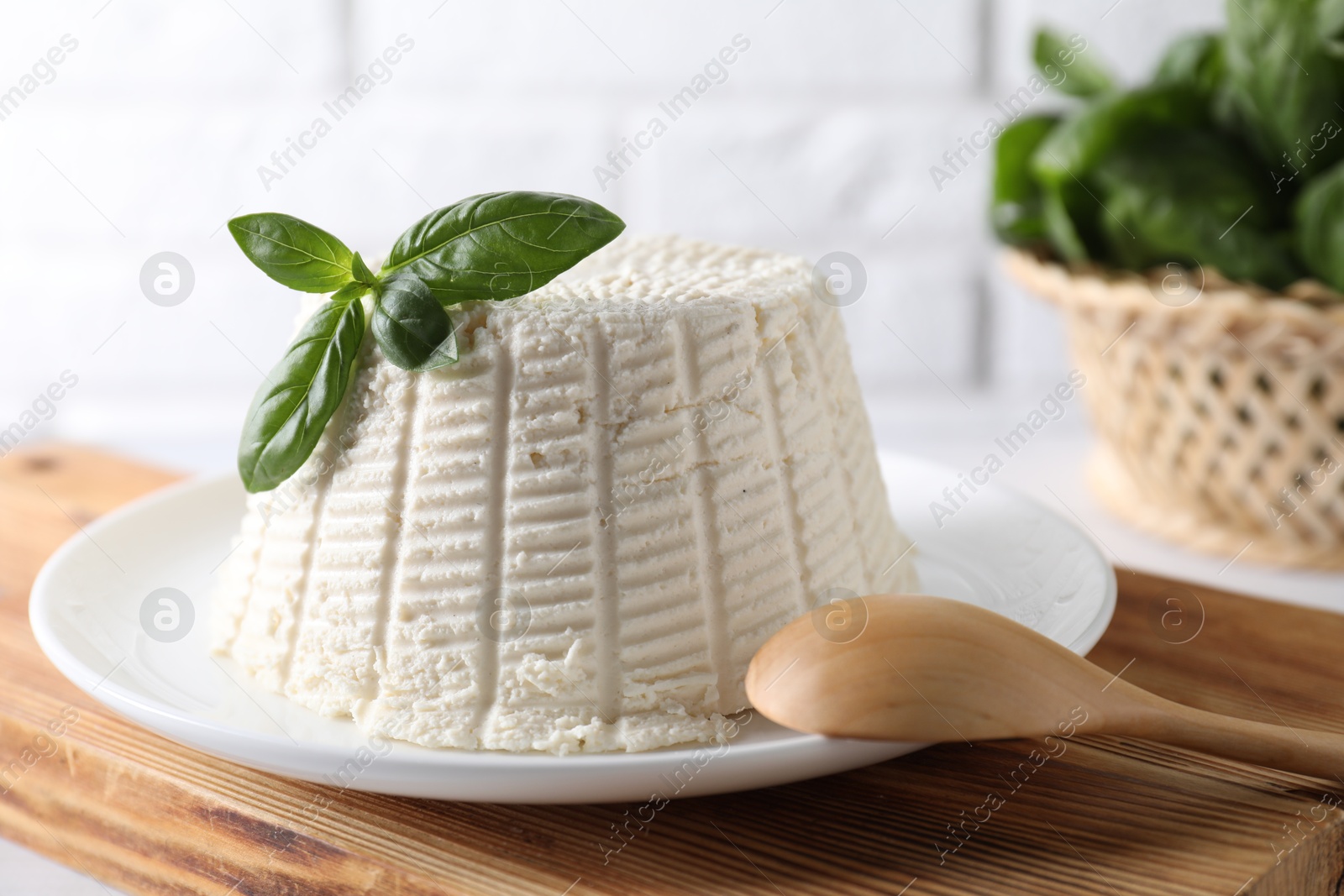 Photo of Fresh ricotta (cream cheese) with basil and spoon on white table, closeup