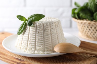 Photo of Fresh ricotta (cream cheese) with basil and spoon on white table, closeup