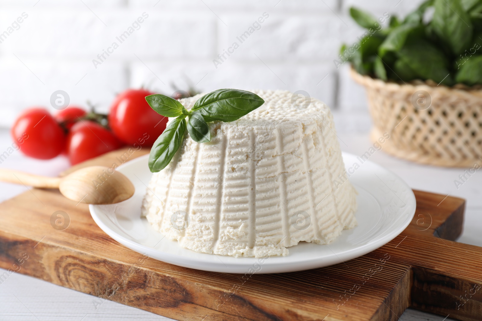 Photo of Fresh ricotta (cream cheese) with basil and spoon on white table