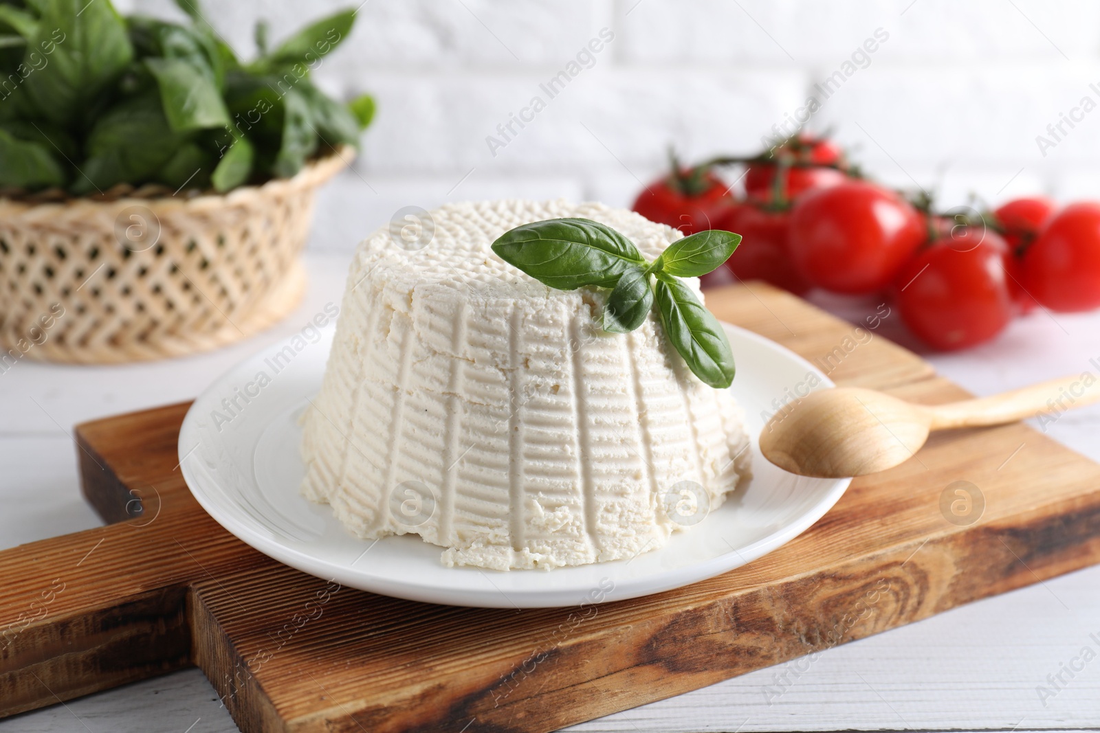 Photo of Fresh ricotta (cream cheese) with basil and spoon on white table