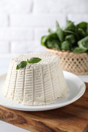 Fresh ricotta (cream cheese) with basil on white table