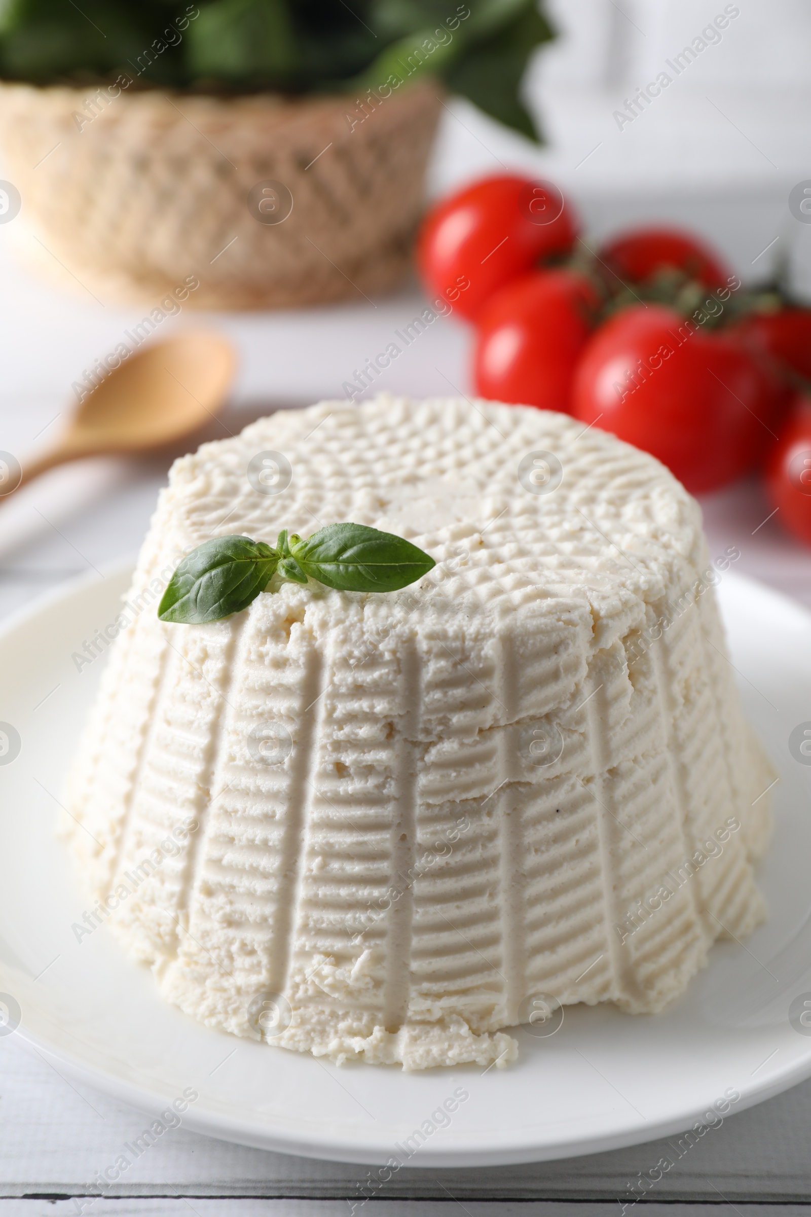 Photo of Fresh ricotta (cream cheese) with basil on white table, closeup