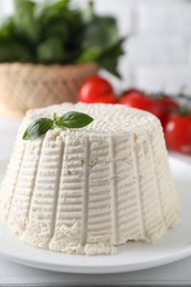 Photo of Fresh ricotta (cream cheese) with basil on white table, closeup