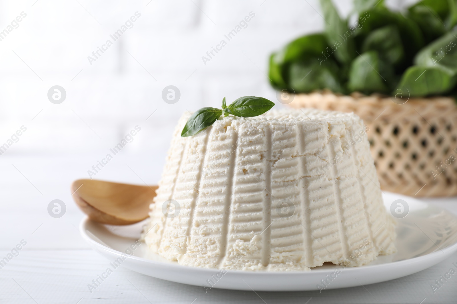 Photo of Fresh ricotta (cream cheese) with basil on white table, closeup