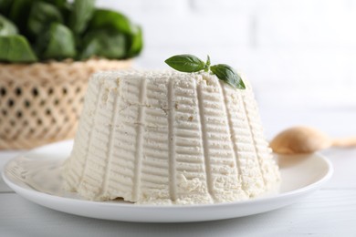 Fresh ricotta (cream cheese) with basil on white table, closeup