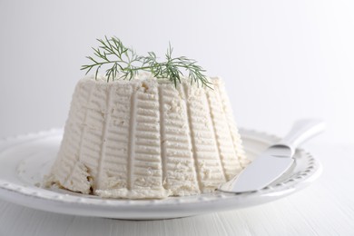 Photo of Fresh ricotta (cream cheese) with dill and knife on white table, closeup