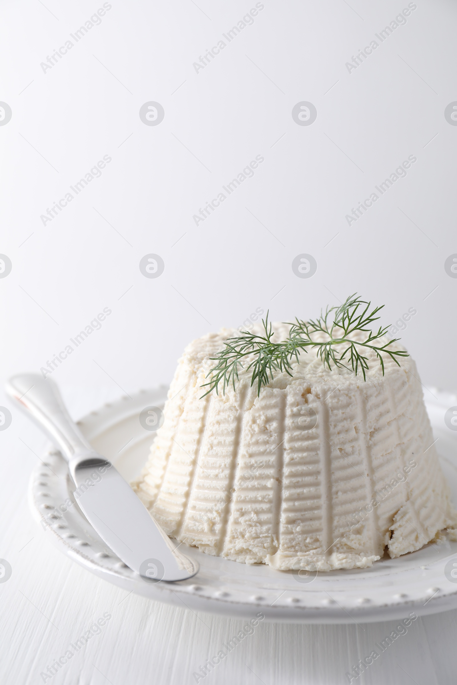 Photo of Fresh ricotta (cream cheese) with dill and knife on white table, closeup