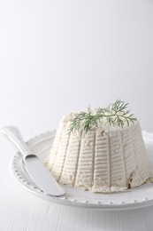 Fresh ricotta (cream cheese) with dill and knife on white table, closeup