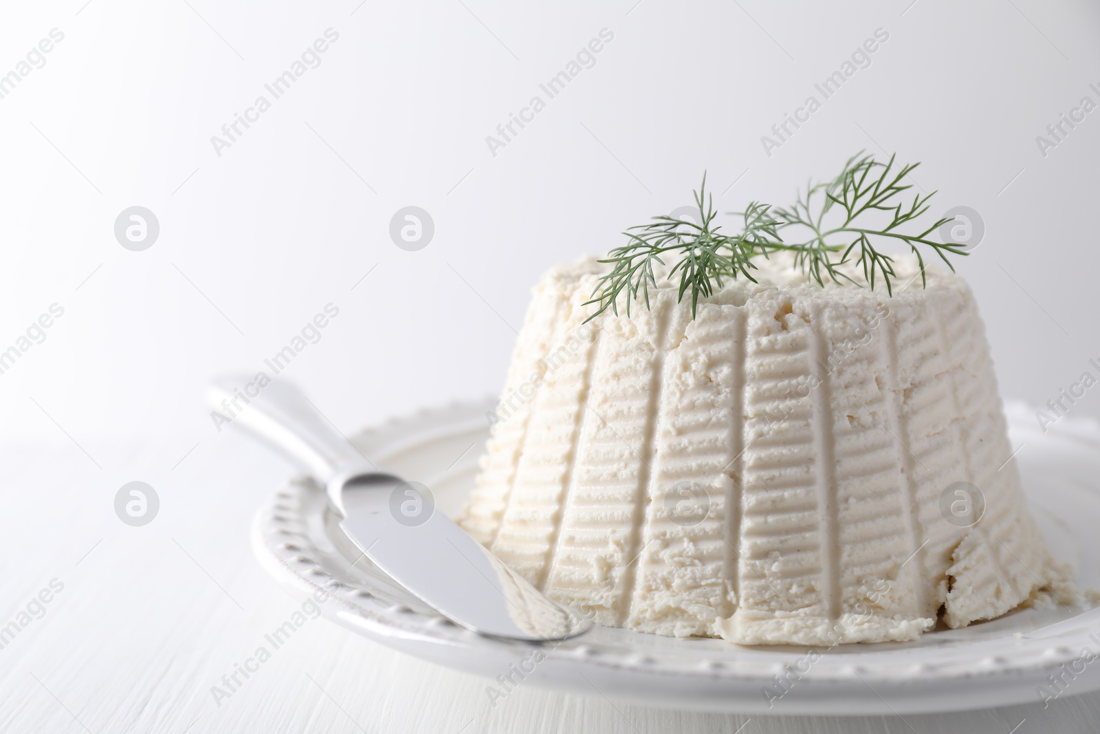 Photo of Fresh ricotta (cream cheese) with dill and knife on white table, closeup