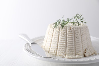 Fresh ricotta (cream cheese) with dill and knife on white table, closeup