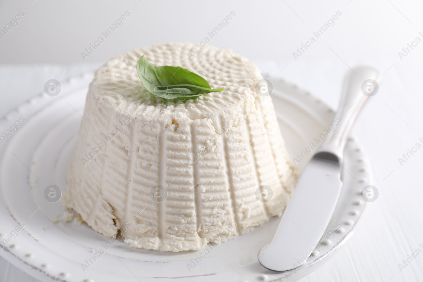 Photo of Fresh ricotta (cream cheese) with basil and knife on white table, closeup