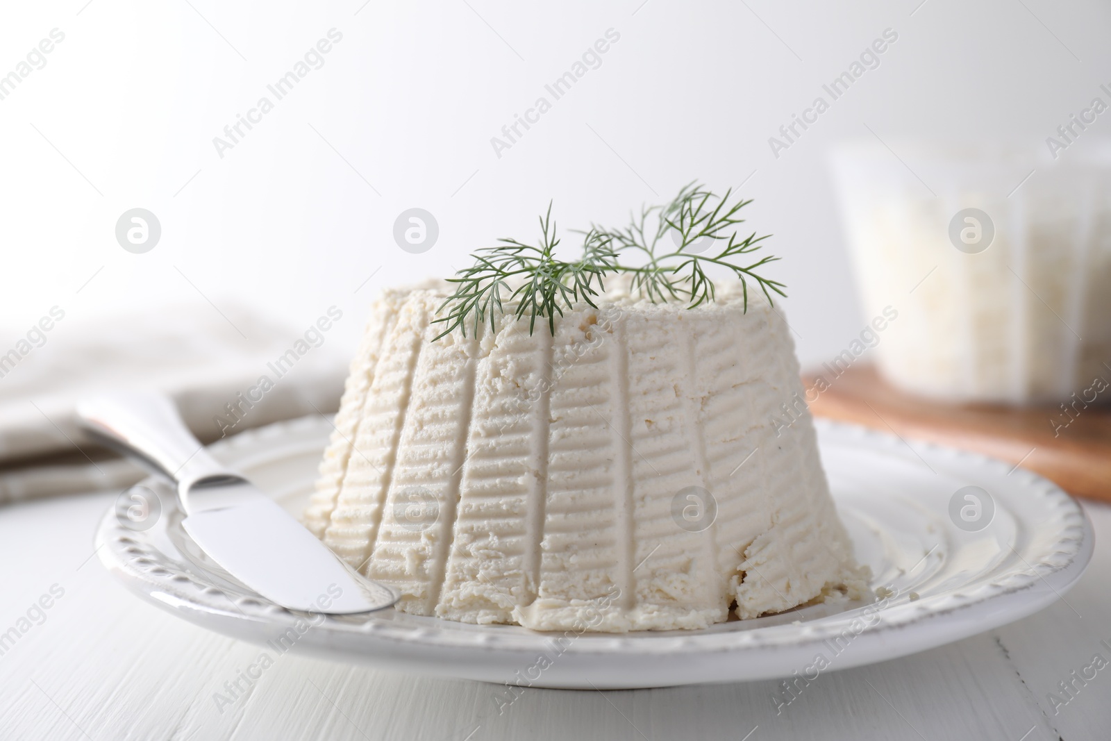 Photo of Fresh ricotta (cream cheese) with dill and knife on white wooden table, closeup