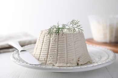 Photo of Fresh ricotta (cream cheese) with dill and knife on white wooden table, closeup