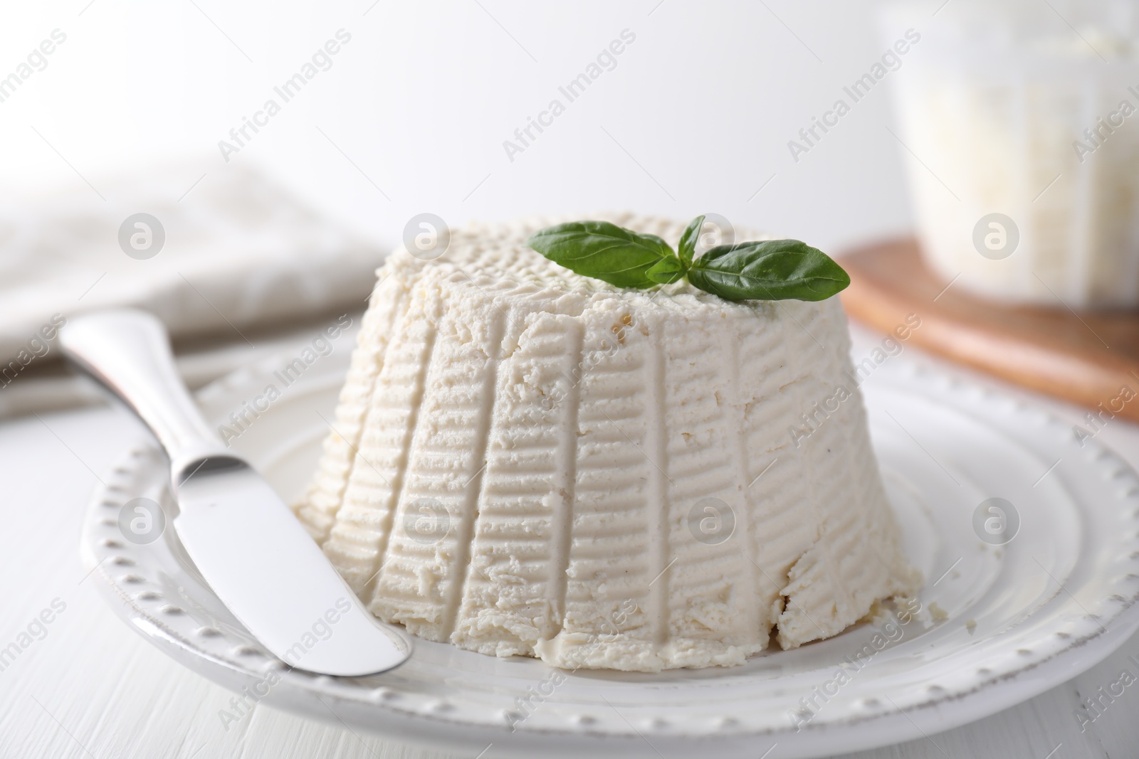 Photo of Fresh ricotta (cream cheese) with basil and knife on white wooden table, closeup