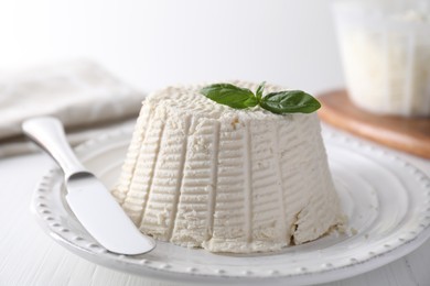 Photo of Fresh ricotta (cream cheese) with basil and knife on white wooden table, closeup