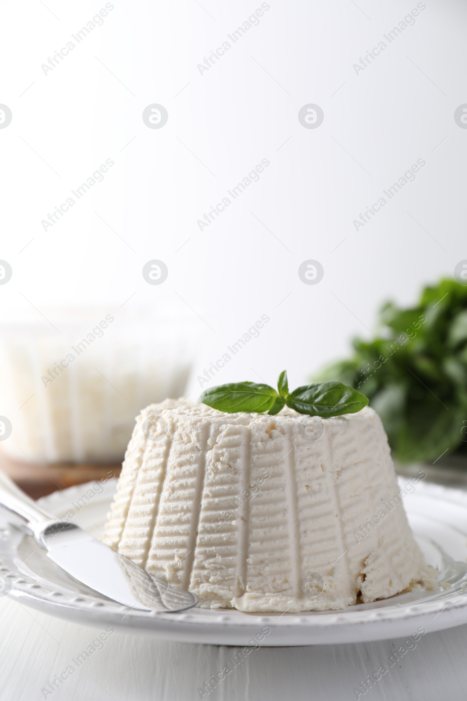 Photo of Fresh ricotta (cream cheese) with basil and knife on white wooden table