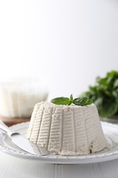 Photo of Fresh ricotta (cream cheese) with basil and knife on white wooden table