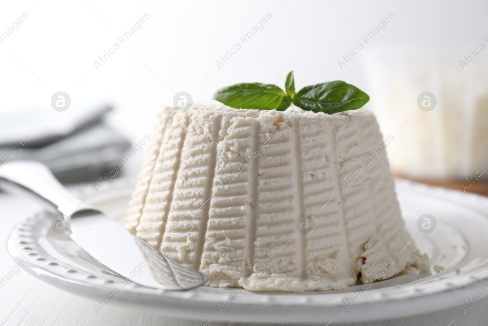 Photo of Fresh ricotta (cream cheese) with basil and knife on white table, closeup