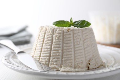 Photo of Fresh ricotta (cream cheese) with basil and knife on white table, closeup