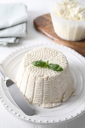 Photo of Fresh ricotta (cream cheese) with basil and knife on white table